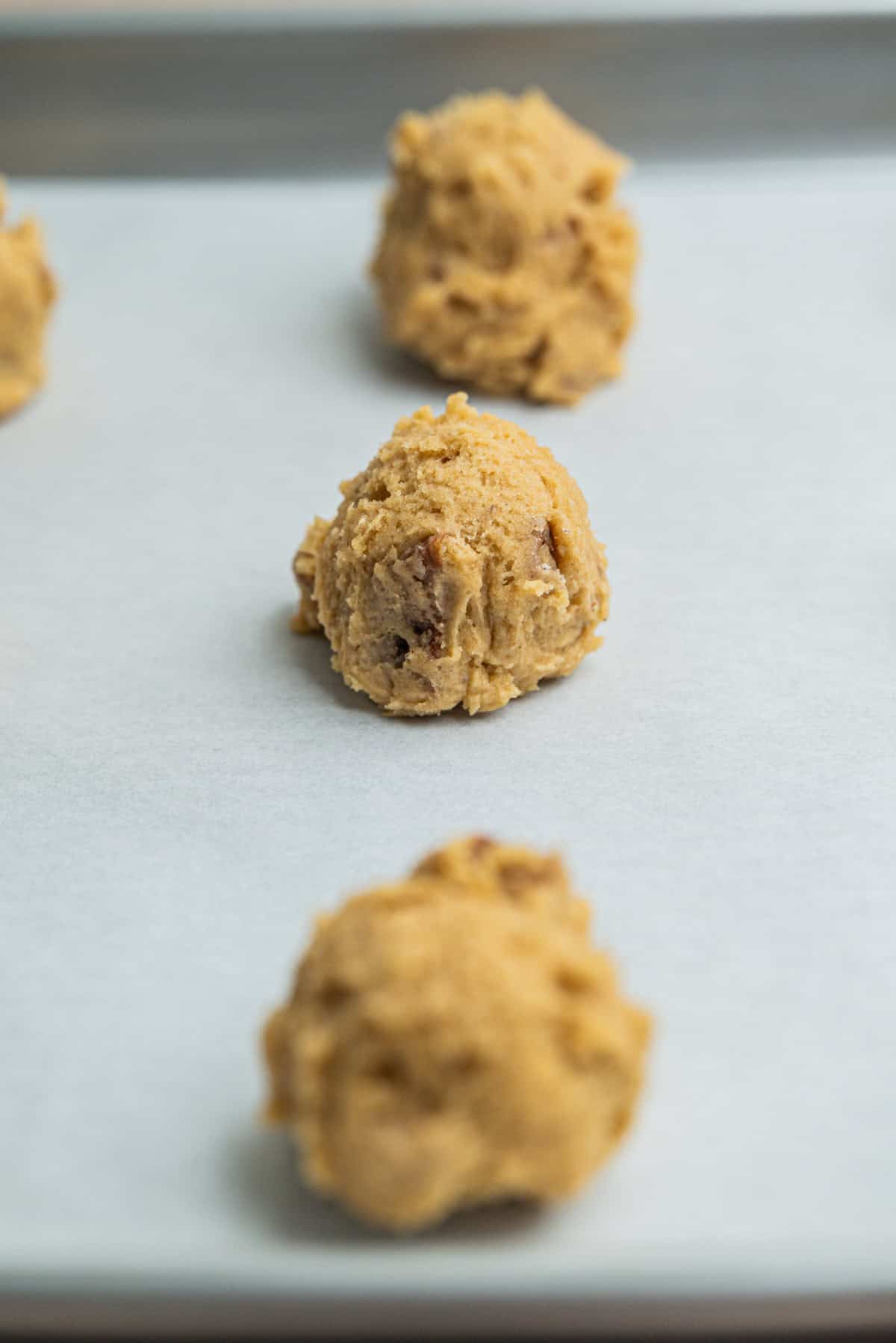 Three scoops of cookie dough placed on a parchment-lined baking sheet, ready to be baked.