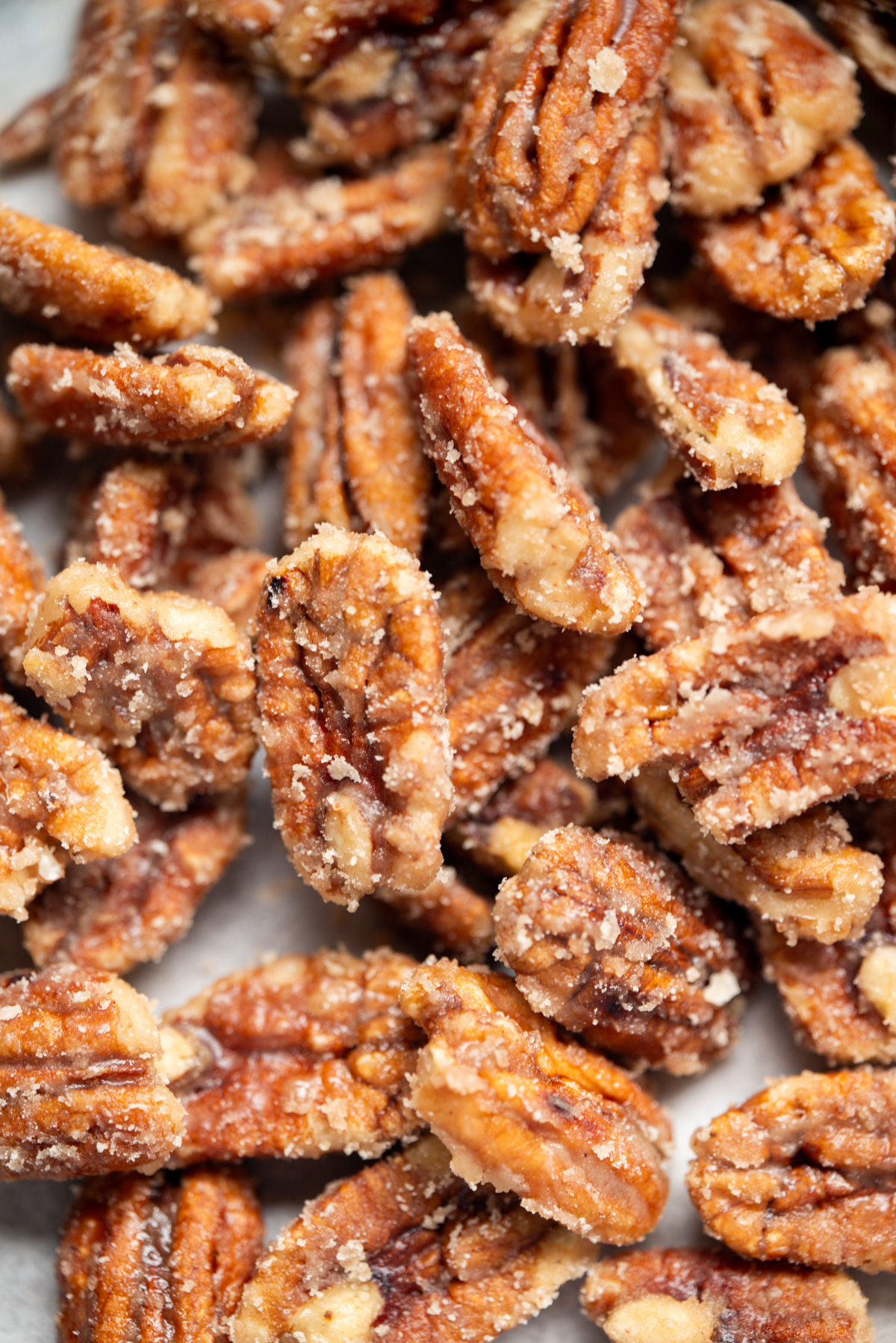 Close-up of sugared pecans, showing their golden-brown color and a crunchy, sugary coating. The pecans are clustered together, highlighting their textured surfaces and sweet glaze.