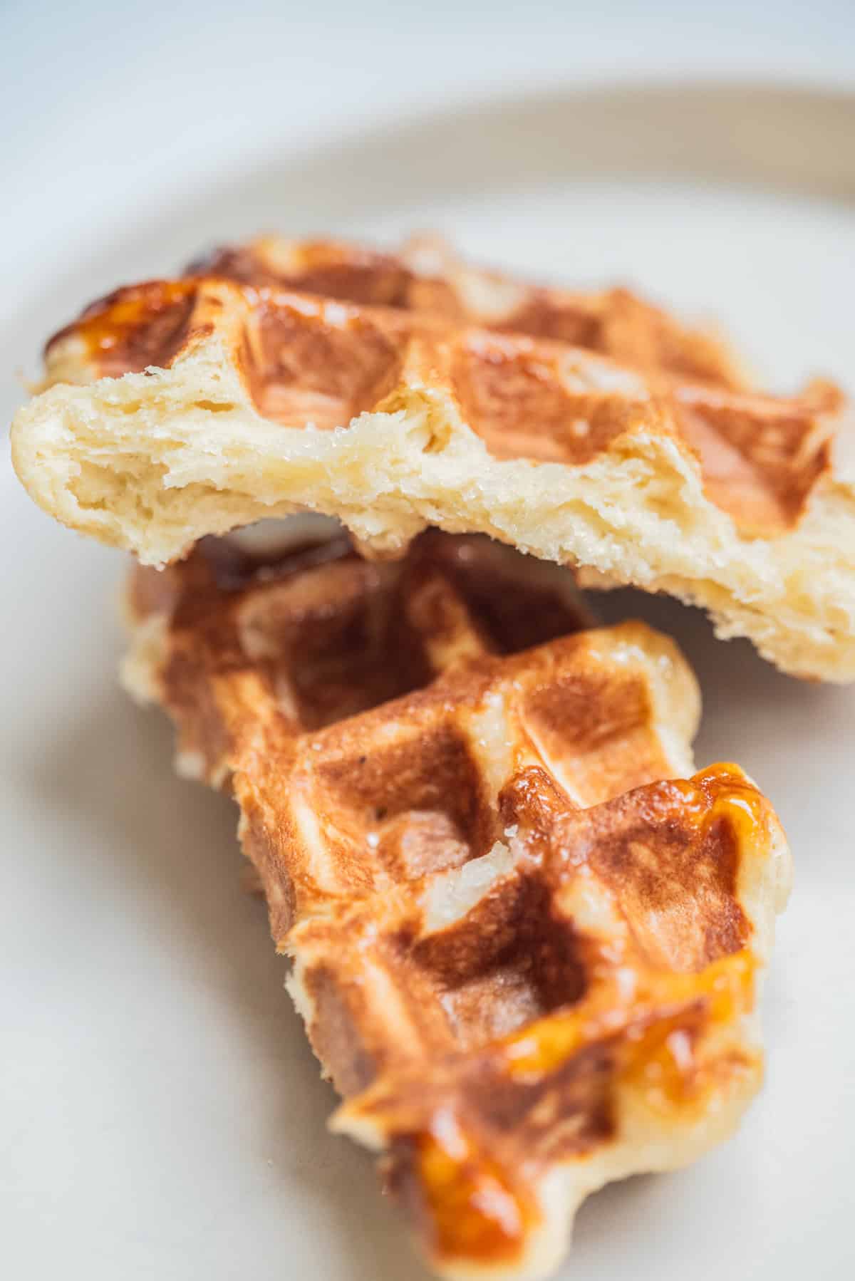 Two pieces of golden, crispy Leige waffles stacked on a white plate, showing their fluffy interior and browned exterior.