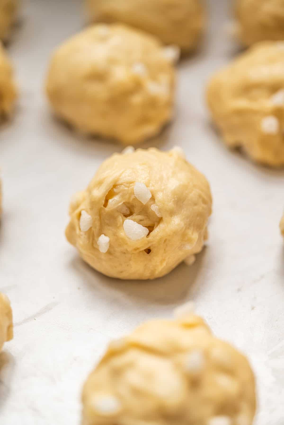 Close-up of raw dough balls with coarse sugar sprinkled on top, arranged on a baking sheet and ready to be baked.