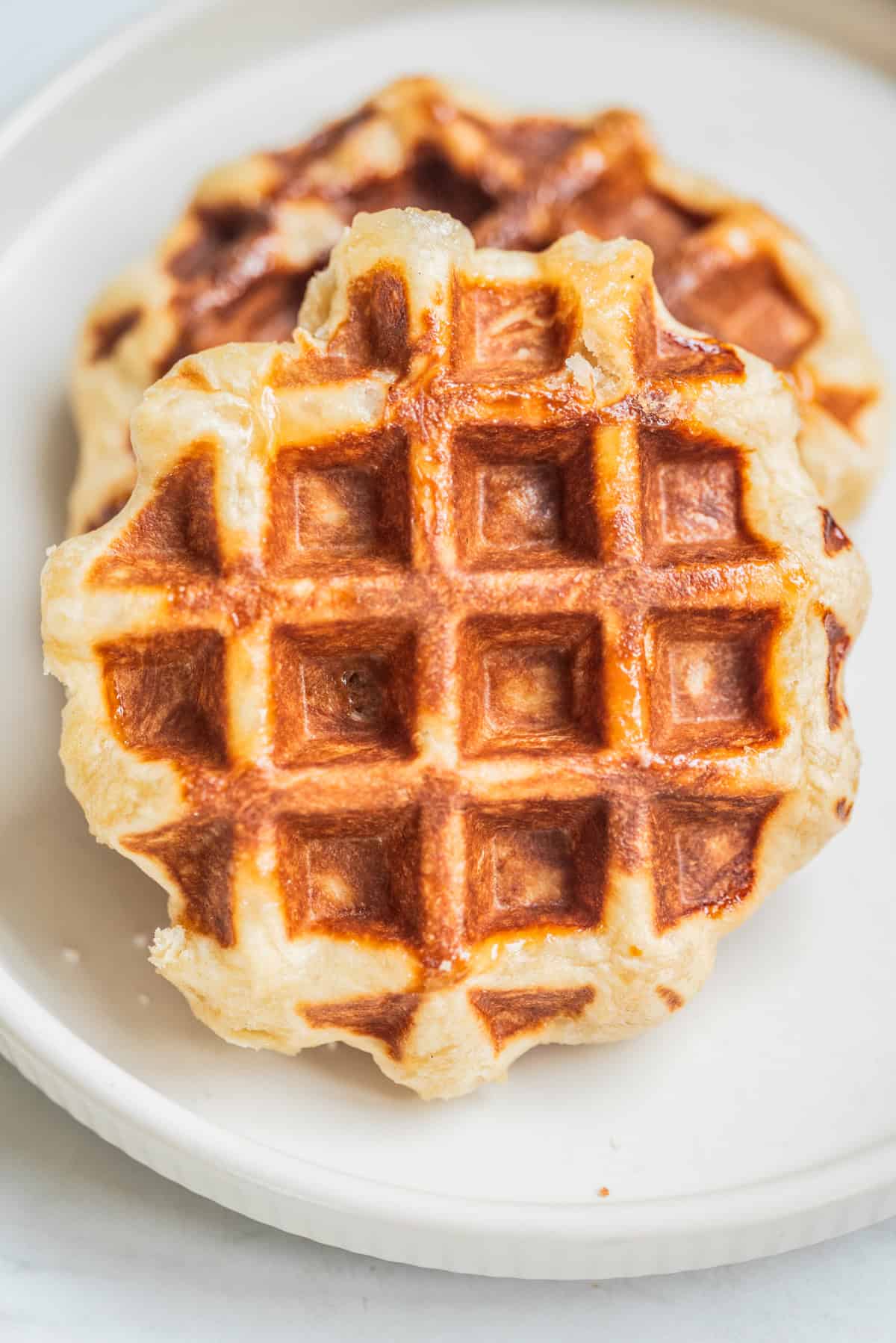 Two golden-brown Belgian Leige waffles stacked on a white plate, showing a crisp, grid-like surface and slightly uneven edges.