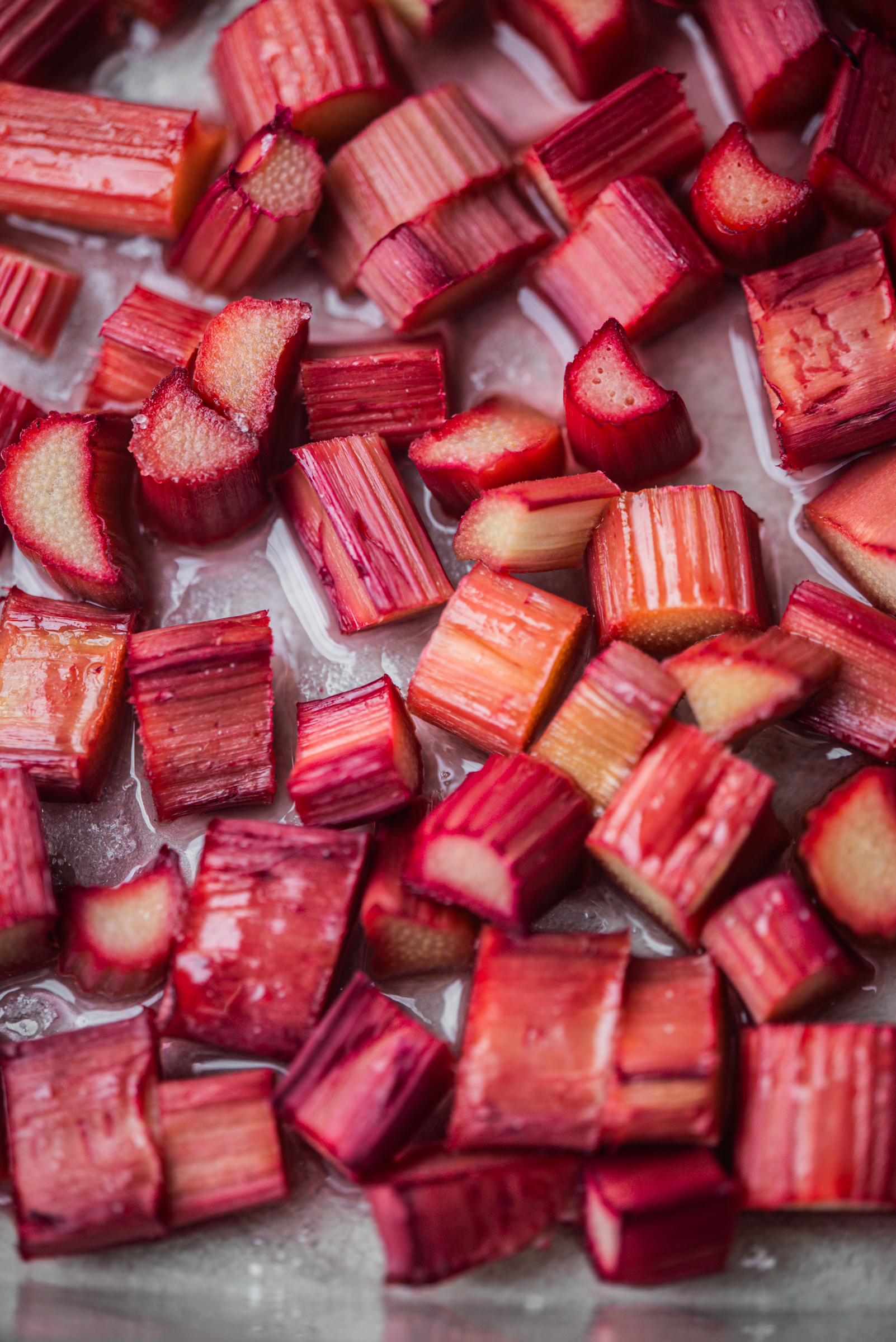 Close-up of freshly cut rhubarb pieces showing their vibrant red and pink hues on a lightly wet surface.