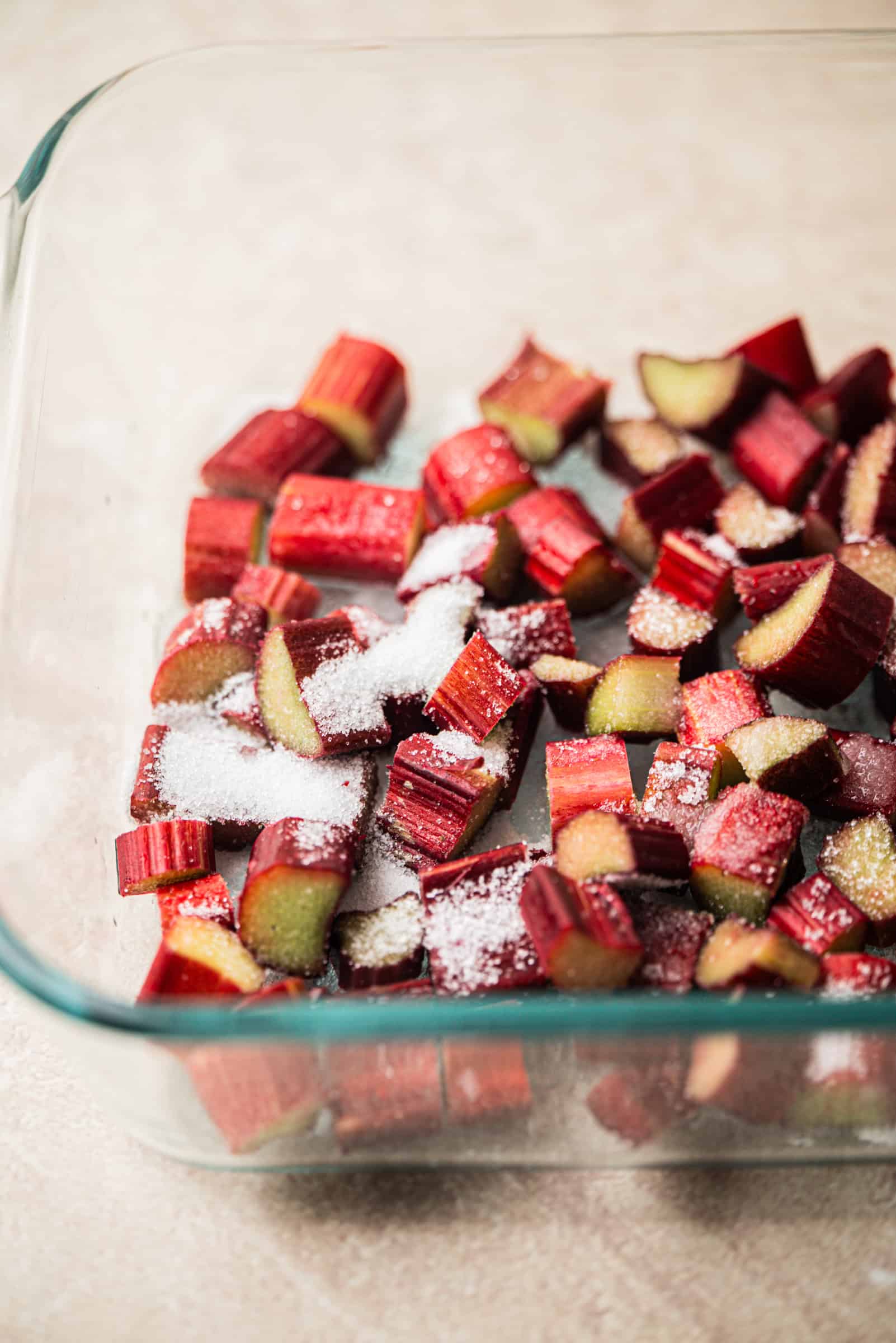 Chopped pieces of rhubarb sprinkled with sugar in a glass baking dish, ready for baking.