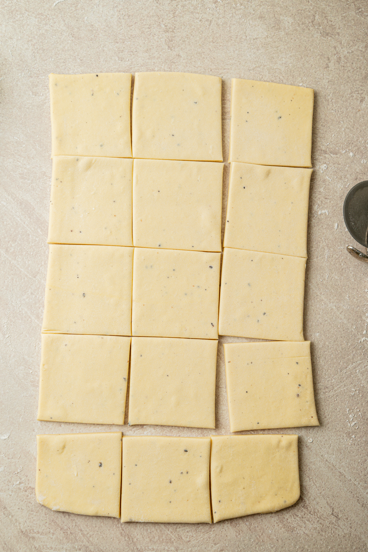 Rectangular sheet of dough cut into fifteen even squares, arranged on a light-colored surface with a pastry cutter visible on the right side.