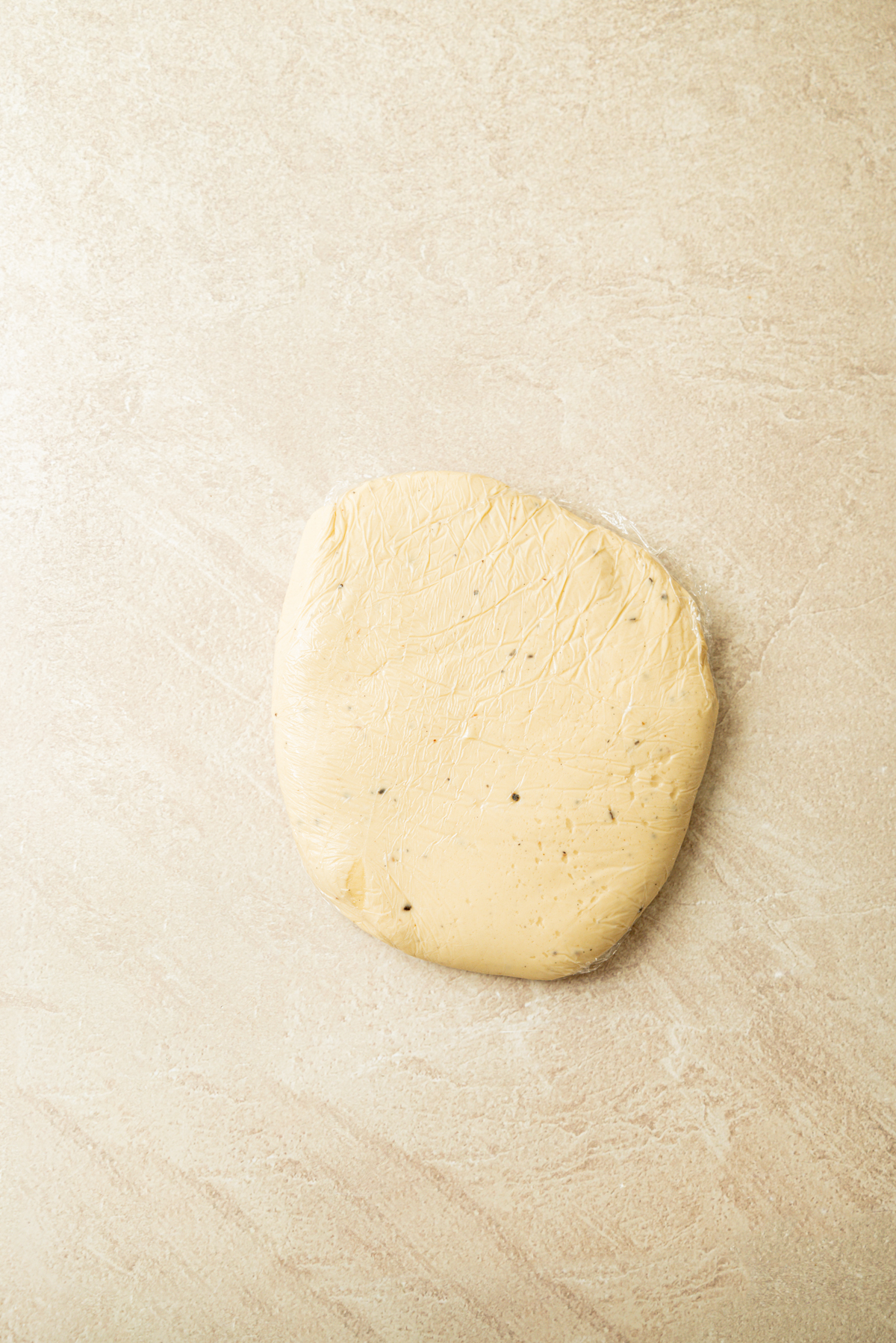 A round, flattened disc of beige dough with a few visible specks rests on a light, textured surface.