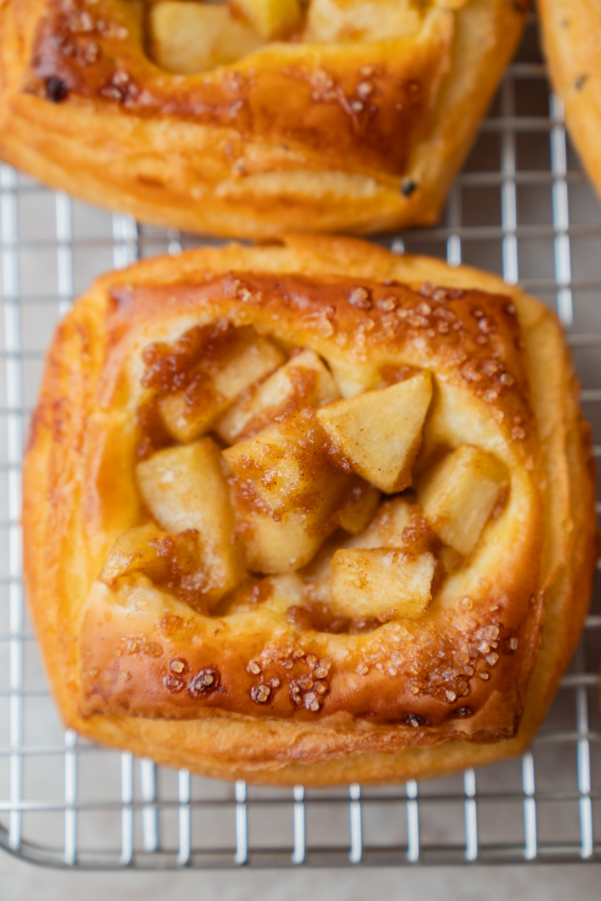 A square apple pastry with golden crust and sugar crystals sits on a wire cooling rack.