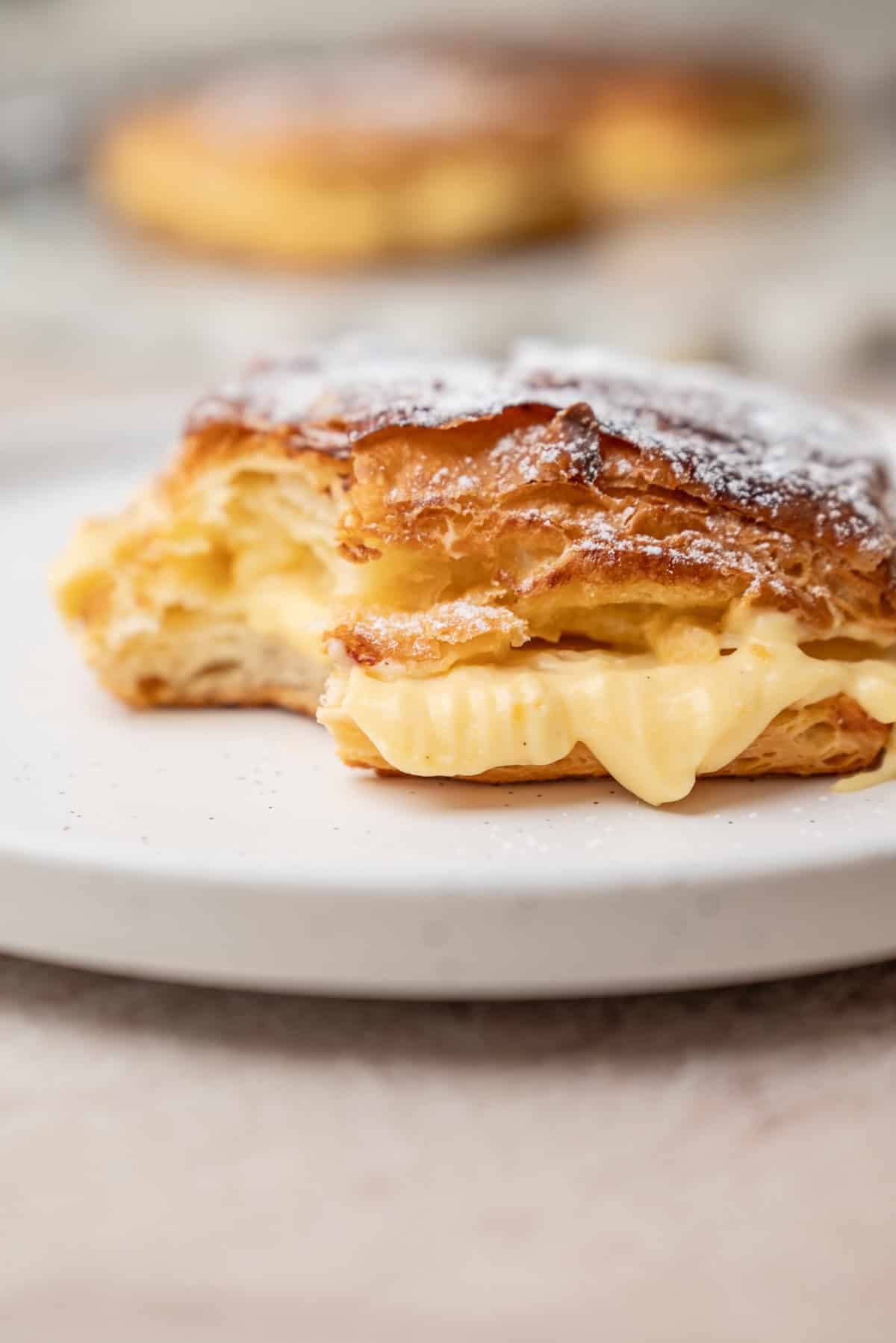 A pastry filled with cream, dusted with powdered sugar, sitting on a white plate.