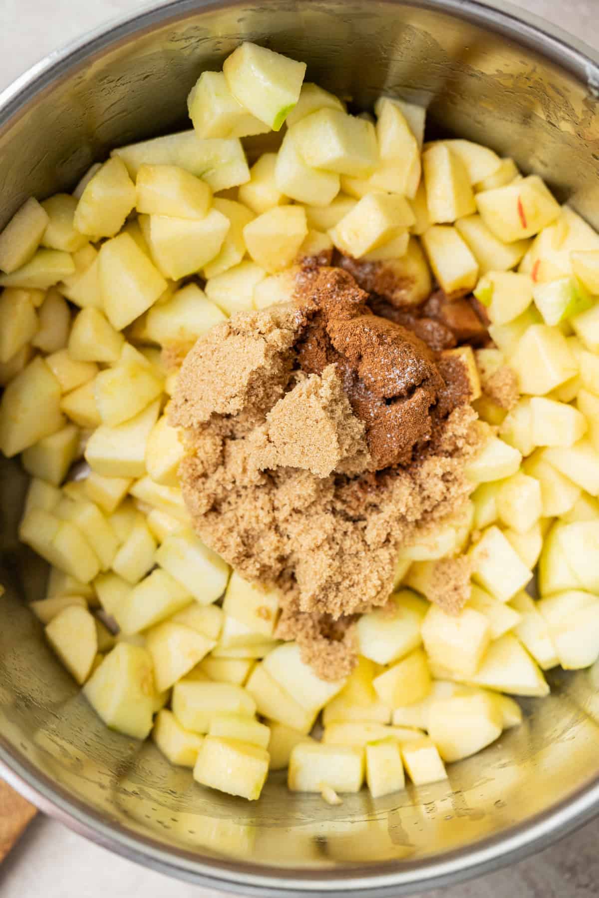 A metal pot filled with diced apples topped with a mound of brown sugar and cinnamon.