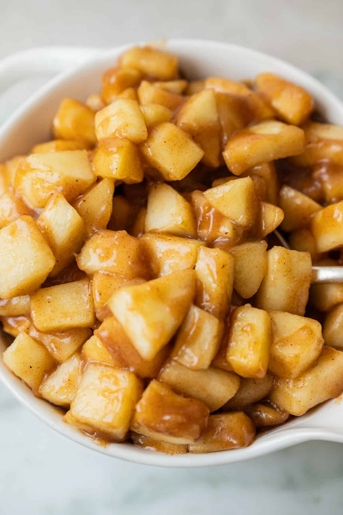 A white bowl filled with diced cooked apples coated in a cinnamon glaze.
