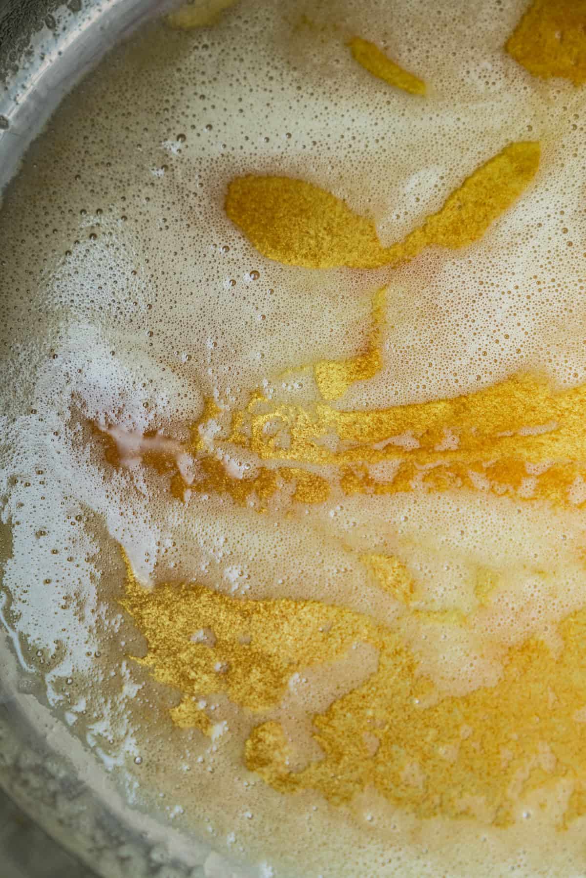Top-down view of melted butter foaming in a pan.