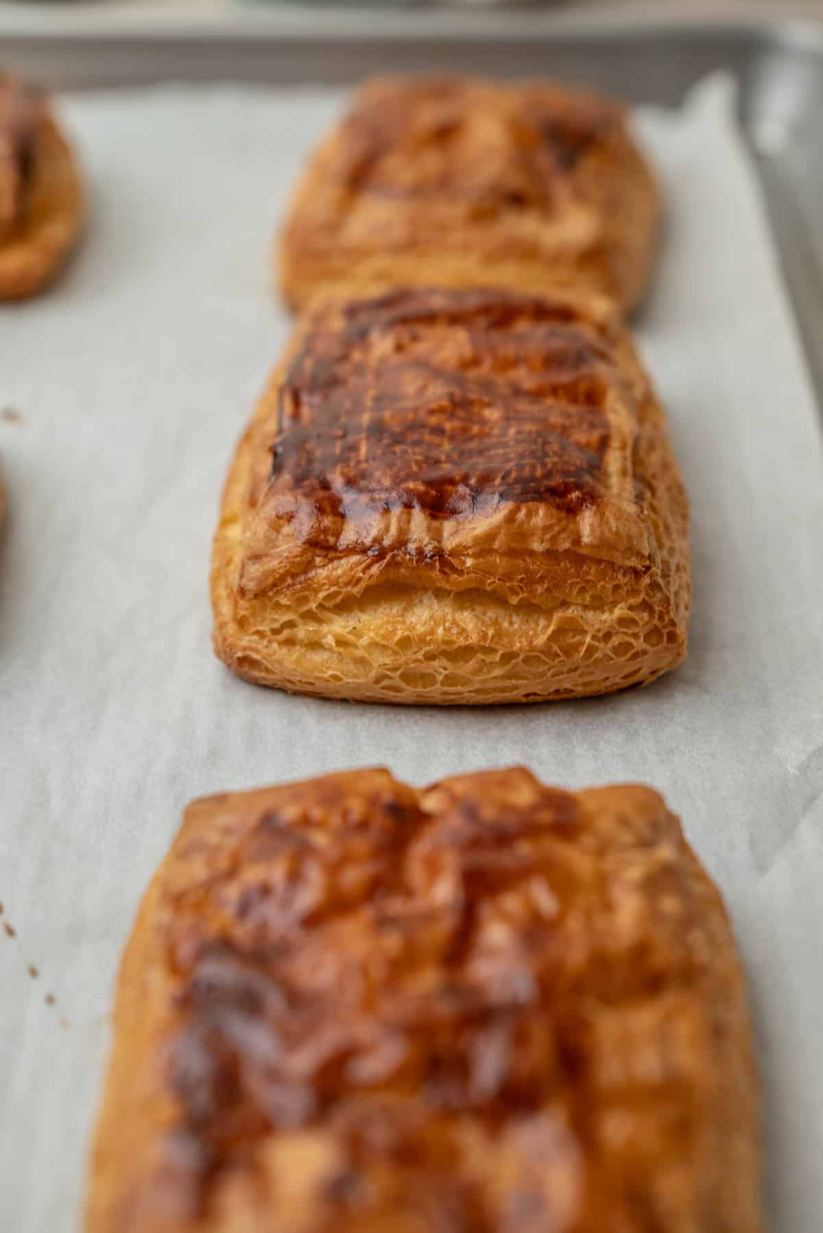 Three golden-brown rectangular pastries on a parchment-lined baking sheet.