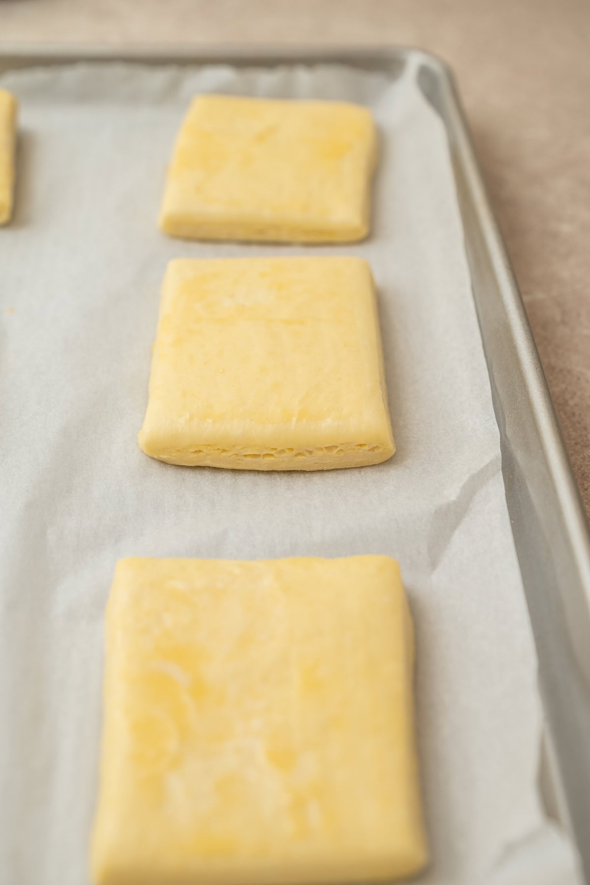 Three unbaked, rectangular pastry dough pieces arranged on a parchment-lined baking sheet.