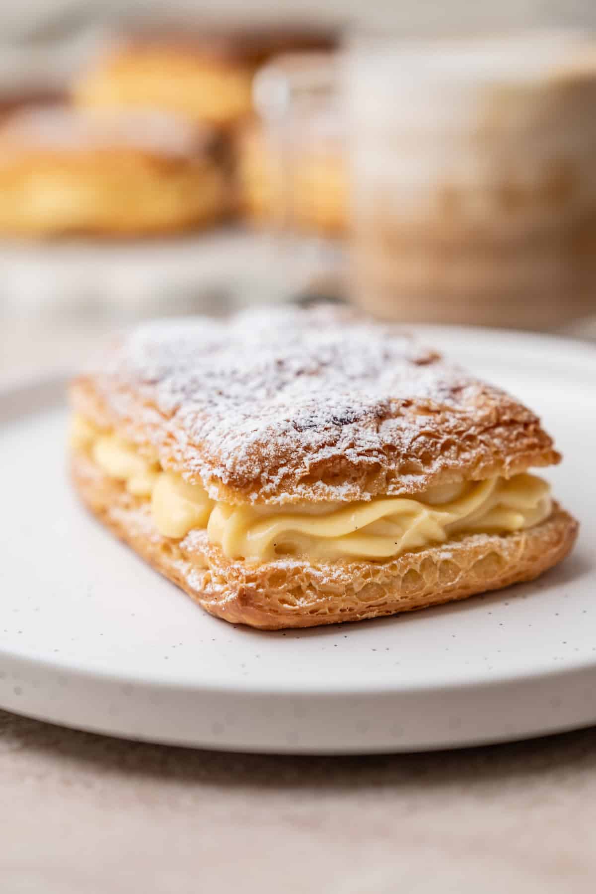A rectangular puff pastry filled with yellow cream and dusted with powdered sugar on a white plate.