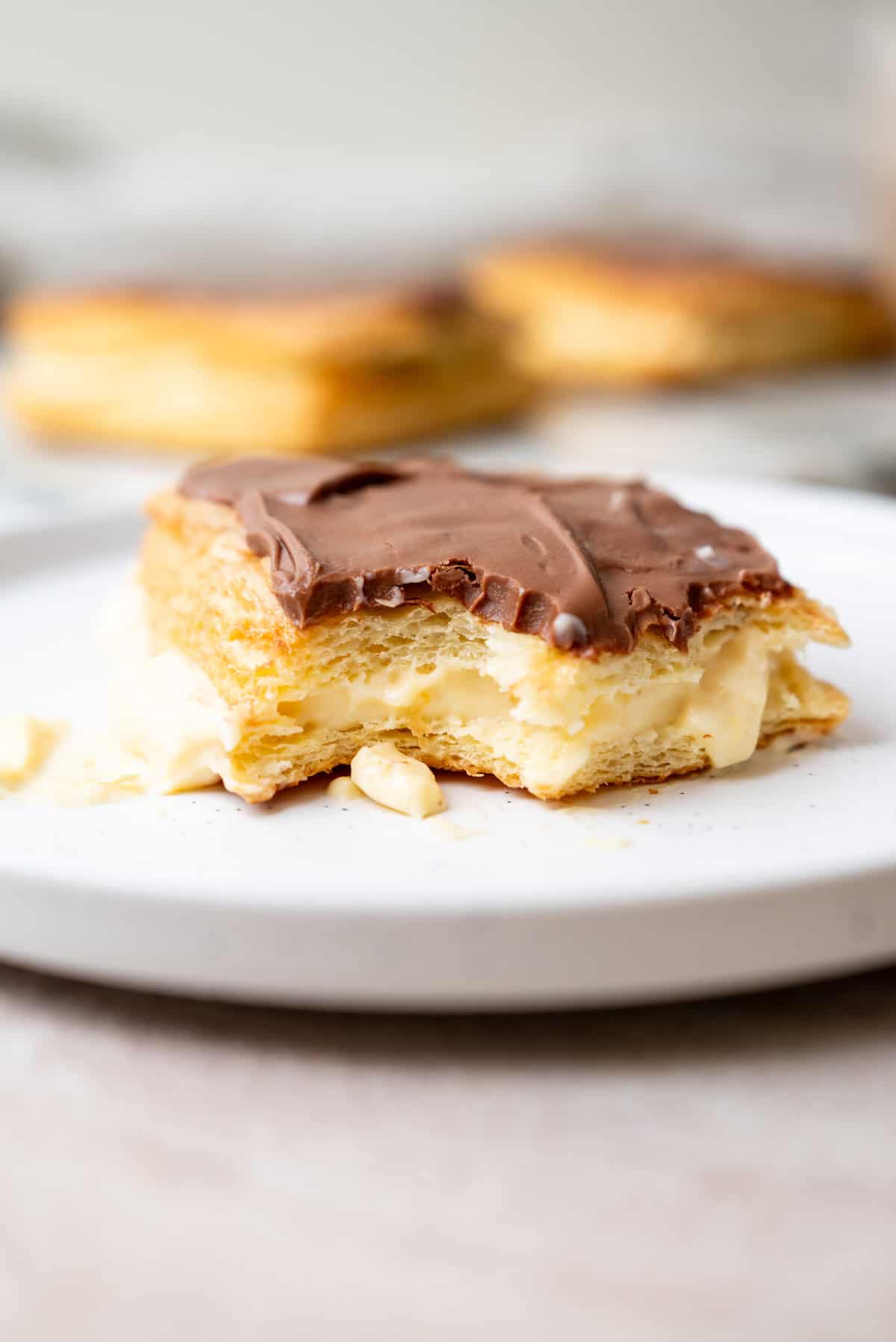 A bitten pastry on a white plate with cream filling and a chocolate glaze top.