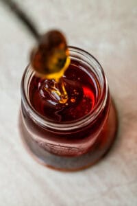 A spoonful of amber syrup drizzling into a small glass jar.