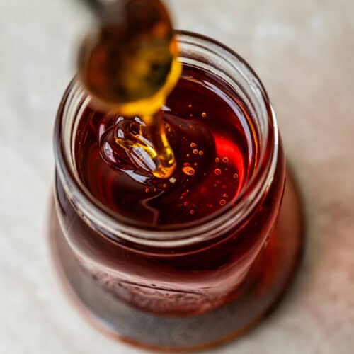 A spoonful of amber syrup drizzling into a small glass jar.