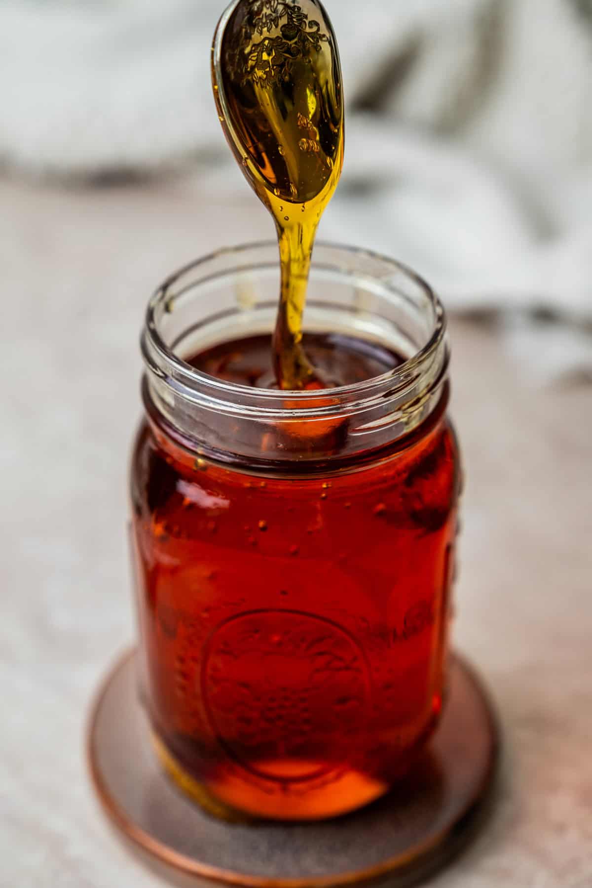 Golden honey drizzling from a spoon into a glass jar.