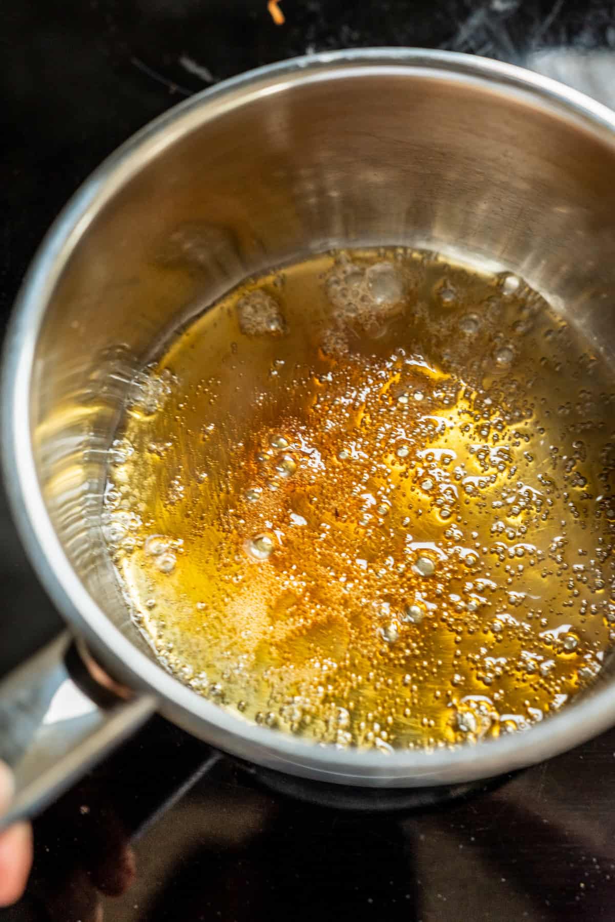 A metal saucepan containing bubbling, golden-brown caramel on a stovetop.
