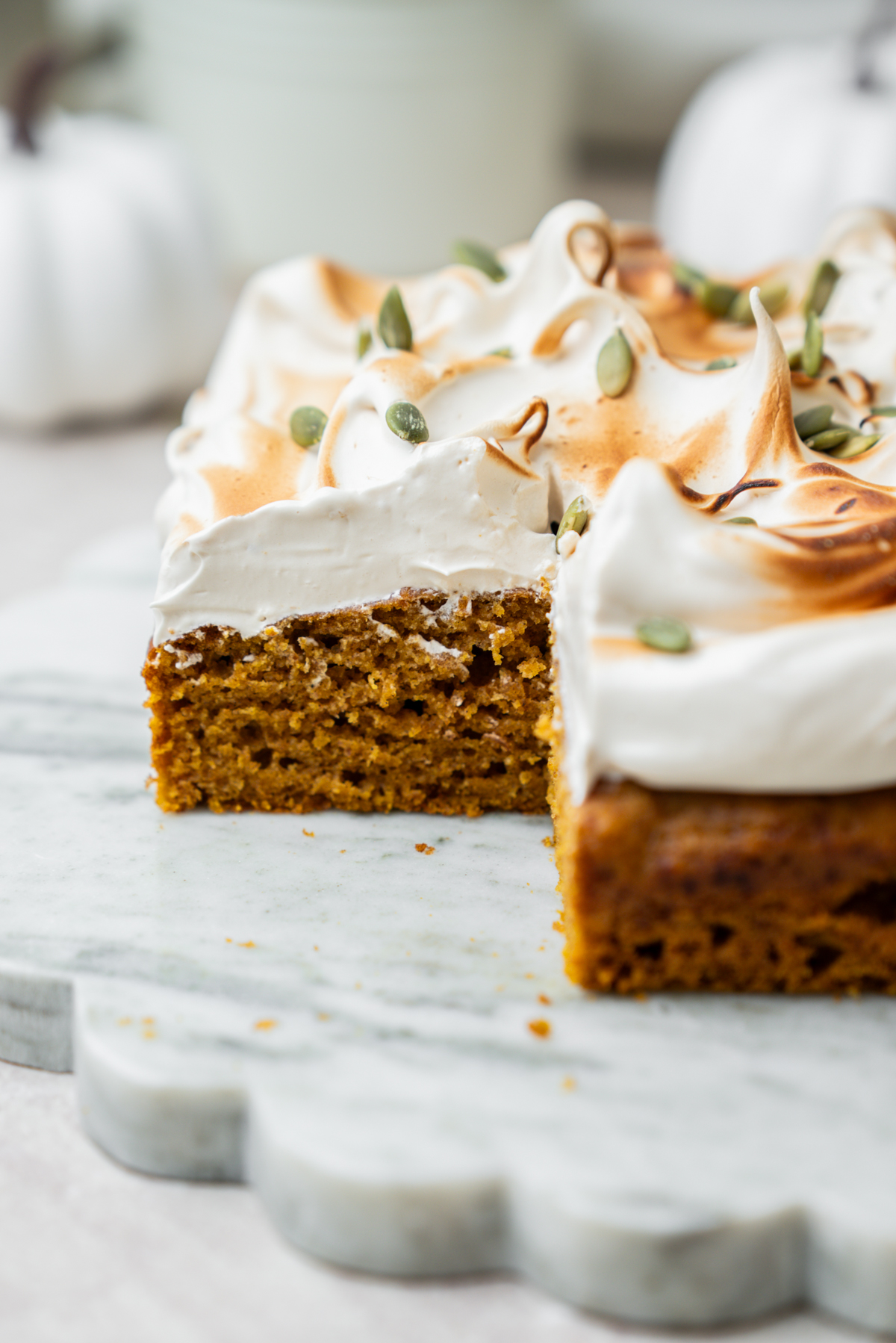 A slice of pumpkin cake topped with toasted meringue and pepitas on a marble platter.