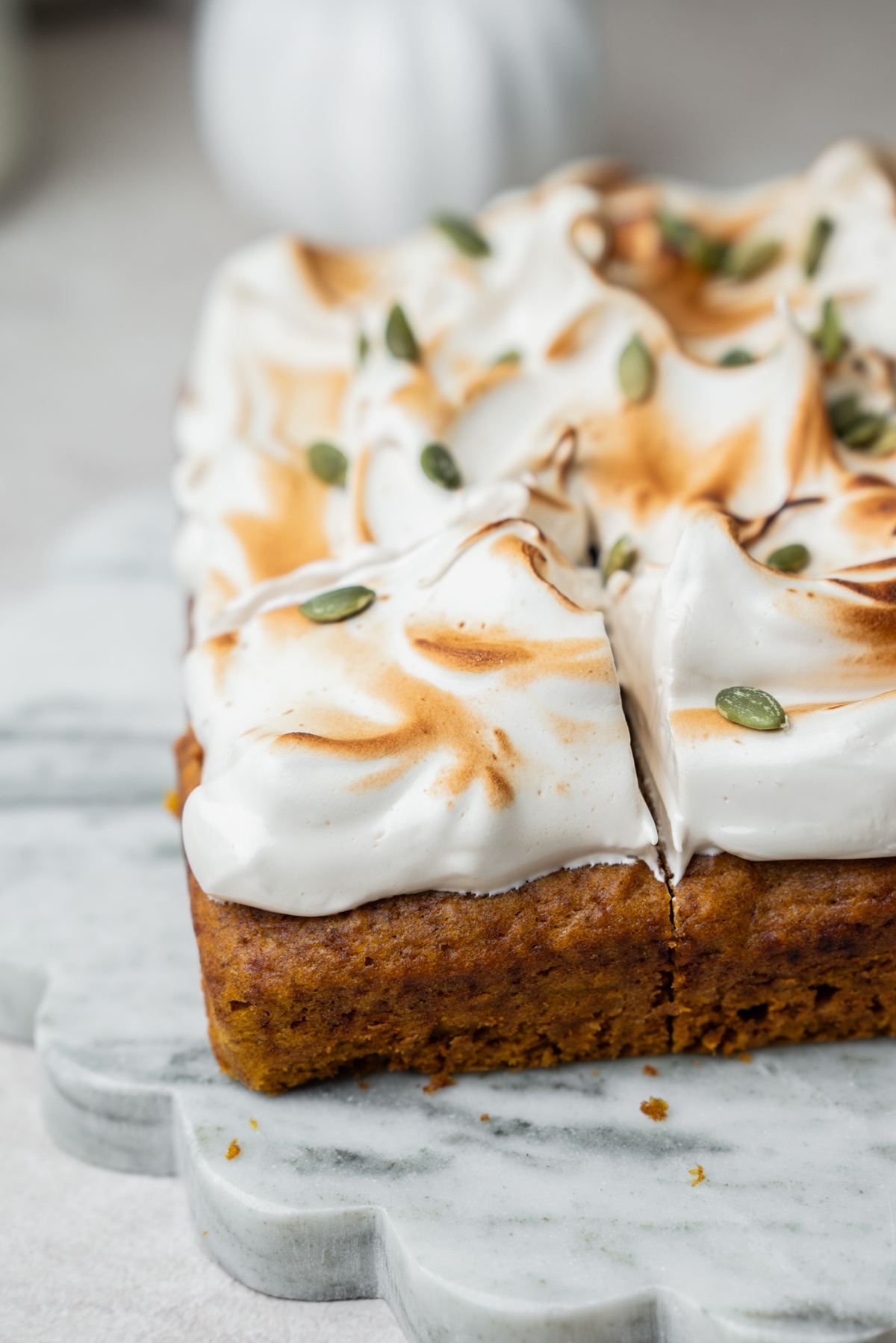 A square slice of pumpkin cake topped with toasted meringue and pumpkin seeds on a marble serving board.