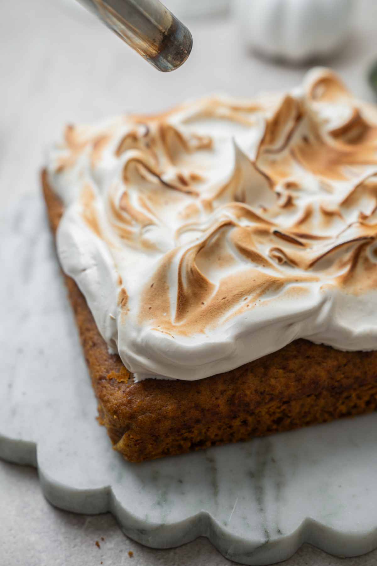 A kitchen torch toasts the meringue topping on a square cake.