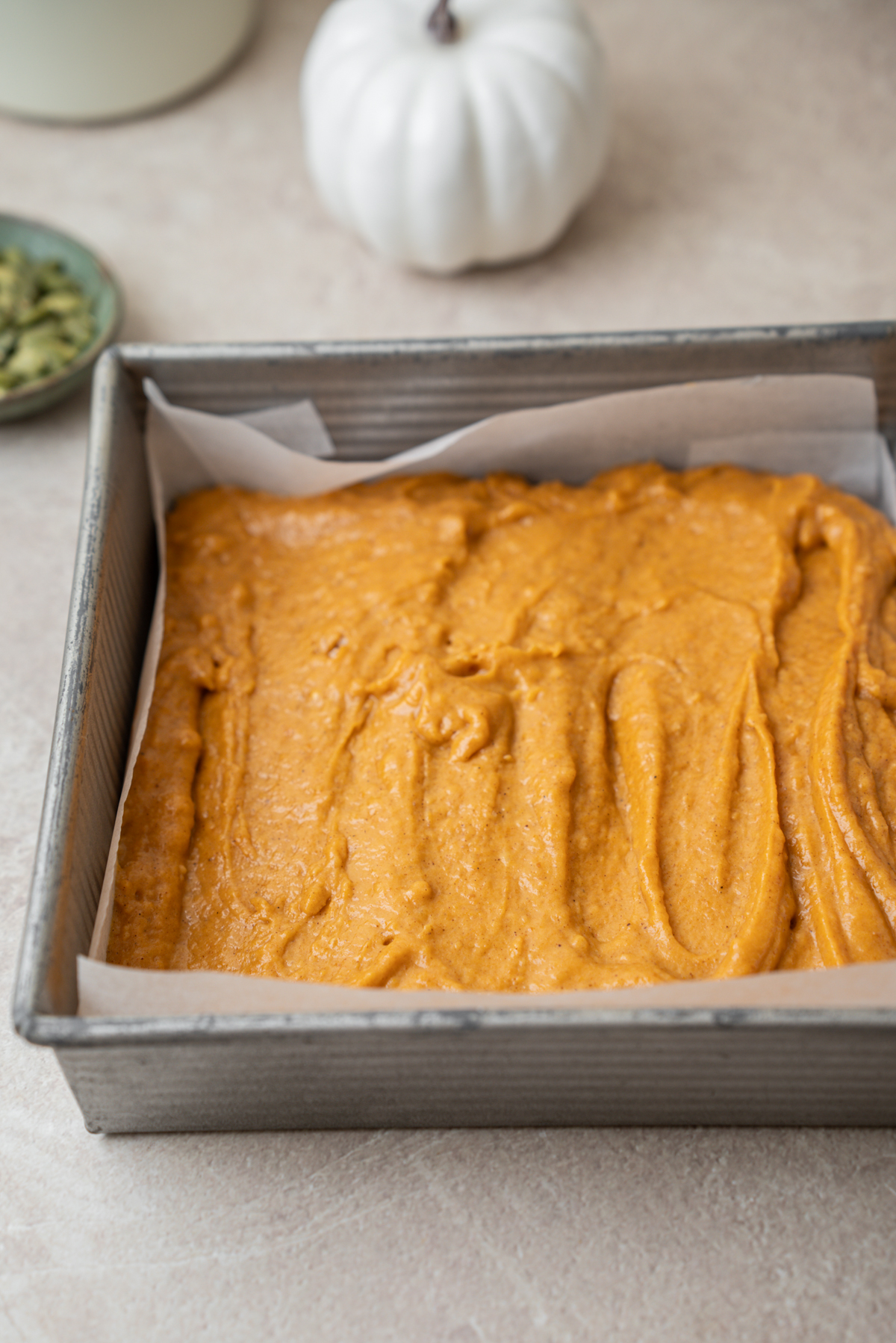 Square metal baking pan lined with parchment paper and filled with raw pumpkin batter.