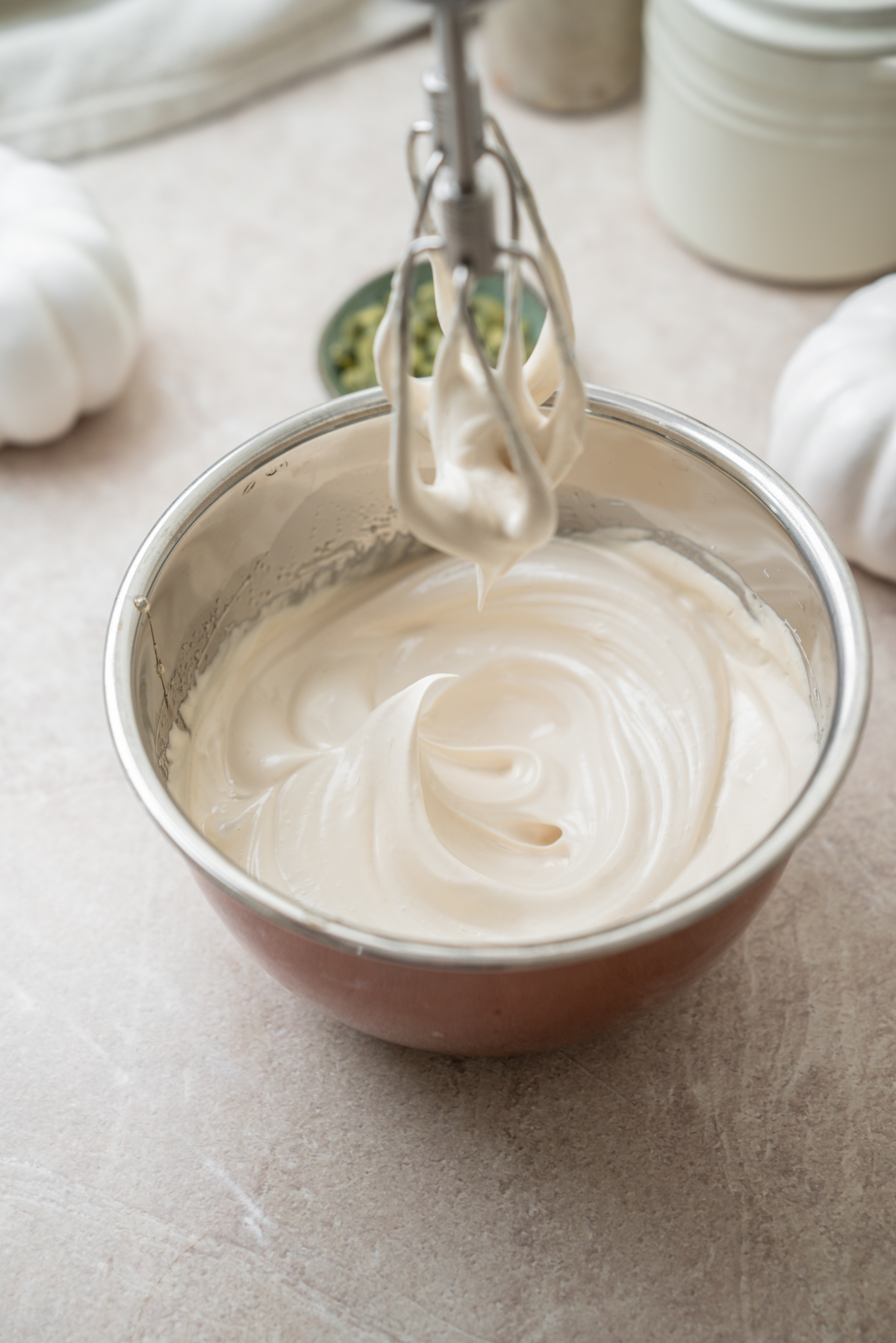 A metal whisk attachment lifts a dollop of thick, white cake batter from a mixing bowl.