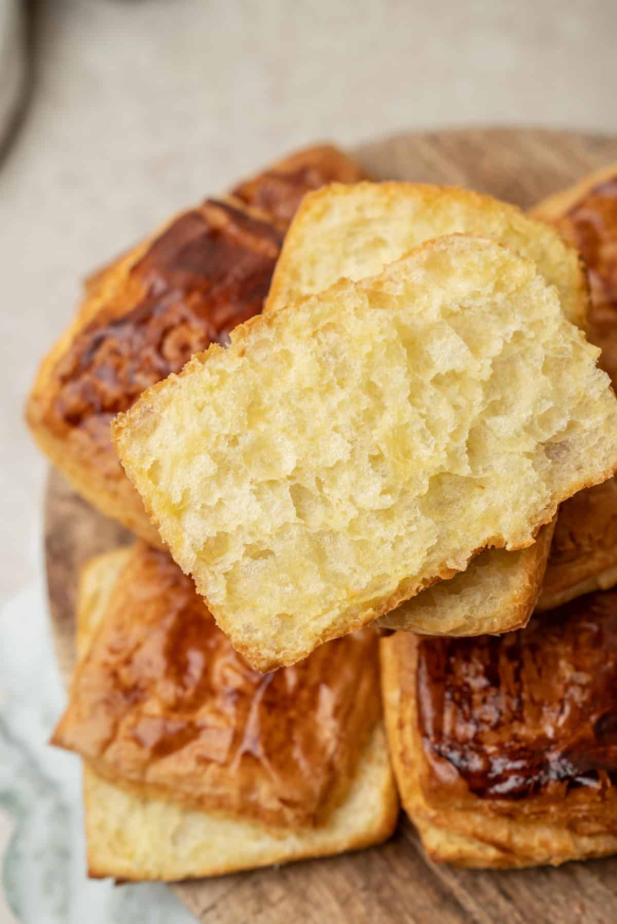A stack of golden-brown pastry squares on a wooden board, with one piece broken in half to show the airy interior.