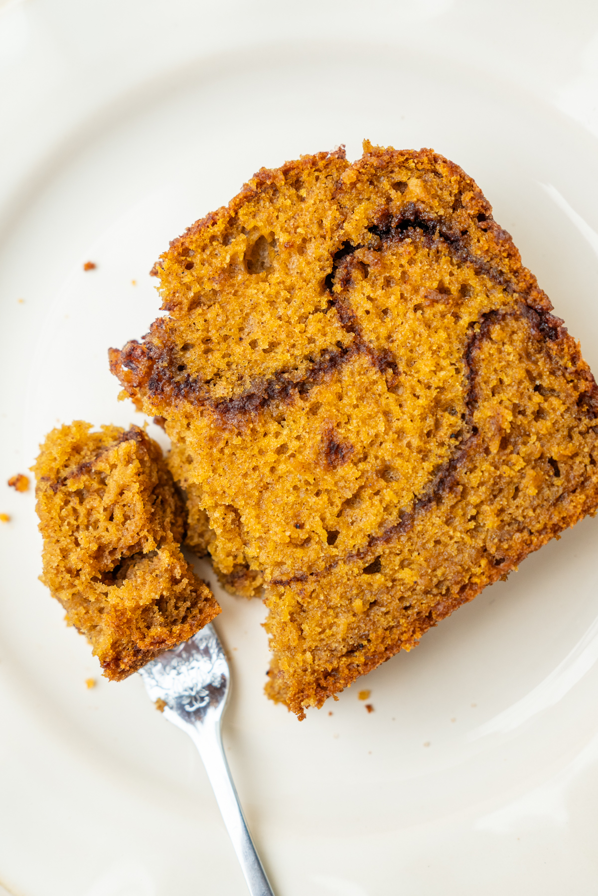 A slice of marbled cinnamon loaf sourdough pumpkin bread on a white plate with a piece broken off on a fork.