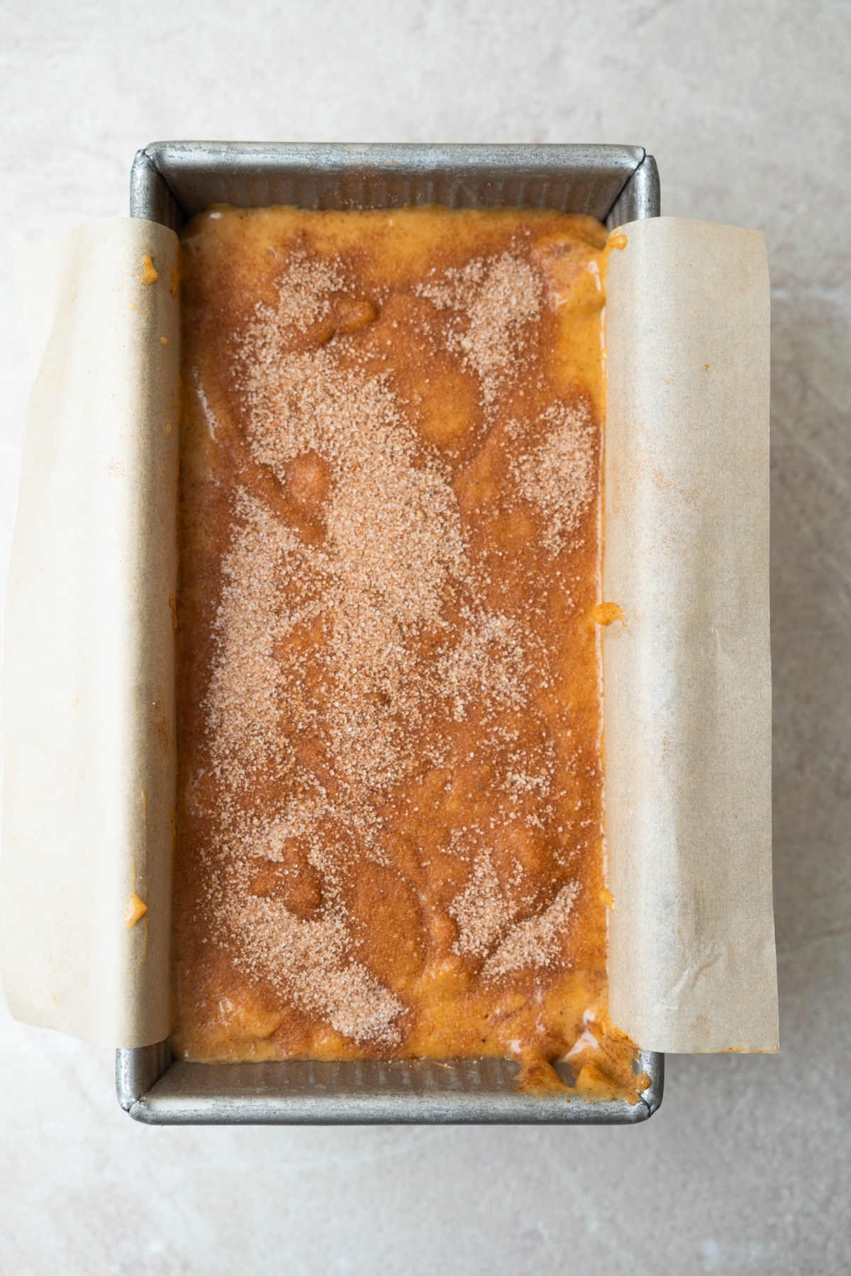 Unbaked quick bread batter in a parchment-lined loaf pan, topped with a dusting of cinnamon sugar.