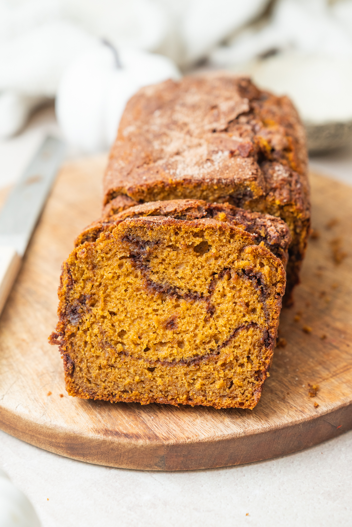 A loaf of pumpkin bread with a cinnamon swirl, sliced on a wooden cutting board.