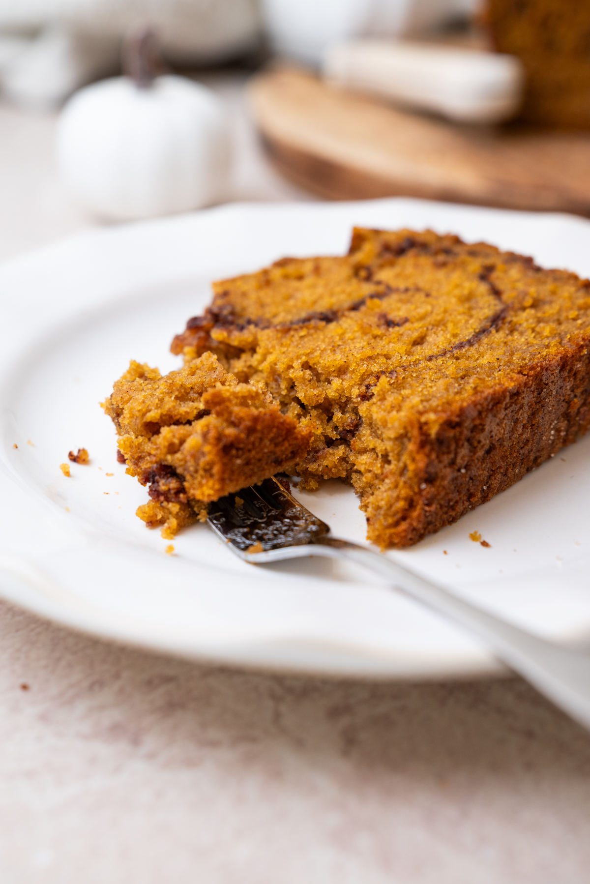 A slice of pumpkin bread with a cinnamon swirl on a white plate, with a fork breaking off a piece.